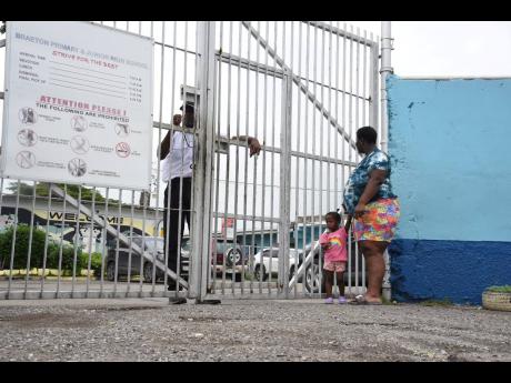 A security officer stands at the gate of Braeton Primary and Infant School, as a parent waits outside. Security has been tightened at the Portmore institution after it was reported that a student was abducted from the school compound, and later found with 
