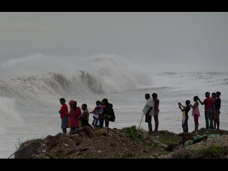 In this October 3, 2016 photo, people stand on the coast on the outskirts of Kingston watching the surf produced by Hurricane Matthew.
