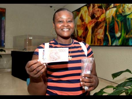 Christine Grant displays one of the new $5000 banknotes, after the Bank of Jamaica officially started distributing the new banknotes to the public yesterday. Grant travelled from Hanover to Kingston in order to be the first in her parish to receive the new