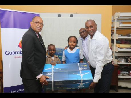 Locksley Stewart (left), senior life advisor, Guardian Life, helps to display one of the industrial fans donated to Siloah Primer School in St Elizabeth yesterday. Also involved in the presentation ceremony are grade one students Mikel Tennant and Sariah F