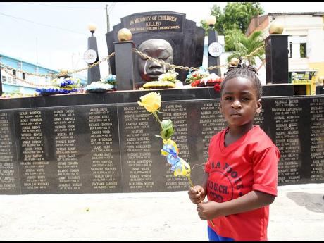 Four-year-old Rushawn Welch, who attends the Sylvia Foote Basic School in Kingston, prepares to lay a rose at the Secret Gardens Monument in downtown Kingston during a wreath laying ceremony to commemorate yesterday’s National Day of Mourning.