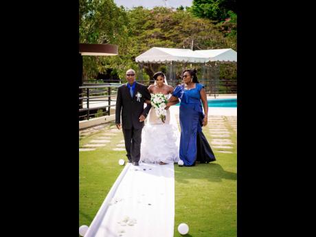 Isheka makes her way up the aisle to her husband, alongside her parents Evans Watson and Hyacinth Gayle-Watson.