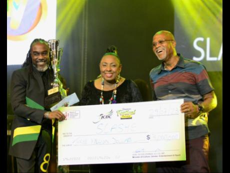 The 2023 Festival Song Competition winner Slashe (left) and producer Donovan Germain (right) receive the winning cheque from Olivia Grange.