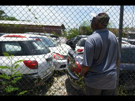 Fredrick Jaskson looks through the fence at Locksley’s Automart and Wrecking Services in St Catherine, trying to see if any of the vehicles recovered belong to him. 