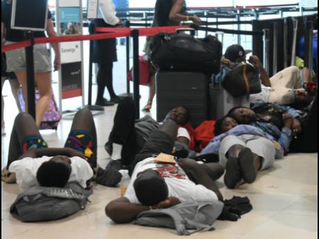 Stranded passengers lie on the floor at the Sangster International Airport amid uncertainty on Thursday as they await news after a disruption in the flight schedule as a result of the closure of the runway.