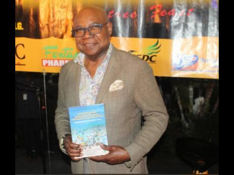 Tourism Minister Edmund Bartlett displaying a book he has co-authored with Professor Lloyd Waller.