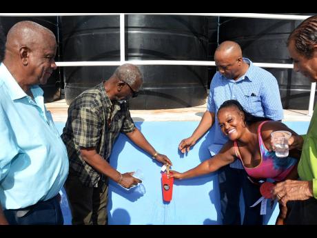 Minister of Local Government and Community Development Desmond McKenzie (second left) assists Fairfield resident, Janique Witter (second right), in filling her container at the commissioning of the $12-million Fairfield water shop in St Elizabeth, on Augus