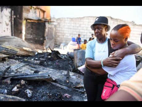 A despondent Carol Dick (left), mother of Latanya Wilson, holds her granddaughter Tobian Graham as she looks at the remains of her home on Rum Lane.