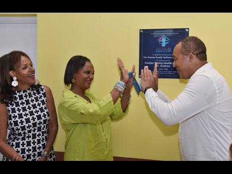 Kim Watson (left) looks on as Dr Christopher Tufton (right), minister of health and wellness and Dr Jacqueline Watson (centre), director, Watson Family RalRosa Foundation, high-five after  unveiling a plaque during the official ceremony for the adoption of