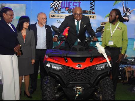 Edmund Bartlett, minister of tourism, uses an ATV bike at the JAMWEST Motorsports & Adventure Park Ltd booth on day two during a tour of the booths at Jamaica Product Exchange (JAPEX) on Tuesday. Also photographed are Jennifer Griffith (left), permanent se