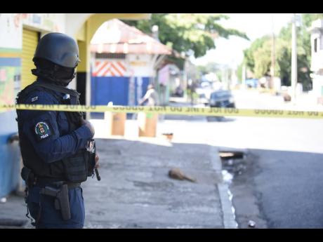 
In this file photo, a policeman stands guard at a crime scene at the intersection of North and Regent streets in Kingston where a man on a motorbike was shot at. 
