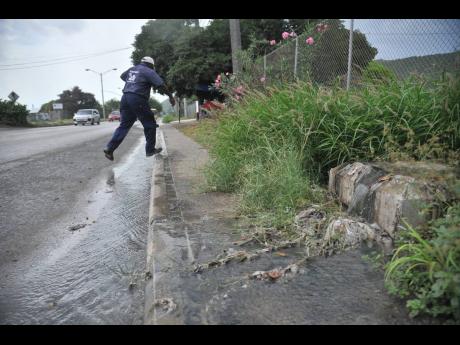 A pedestrian hops back on to the sidewalk after being forced to walk in the road as sewage flowed along Norman Manley Boulevard in Harbour View, St Andrew, on Monday.