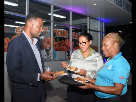From left: David Mullings Jr, senior sales executive, ATL Automotive, and Cheryl Grierson-Bird taste the chicken wings served by Sandra Clarke, manager, Bird Shack, Whitter Village.