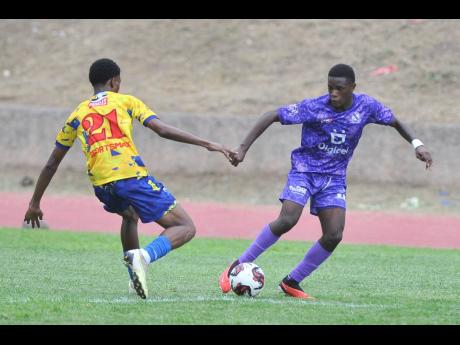 Kingston College’s Alex Hislop attempts to dribble by Hydel High School’s Dontay Stewart during a Manning Cup match at the Stadium East field yesterday. The game was later postponed on account of lightning.