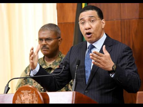 Prime Minister Andrew Holness (right) speaks to the media while Brigadier Markland Lloyd, force executive officer of the Jamaica Defence Force, looks on during a post-Cabinet press briefing at Jamaica House yesterday.