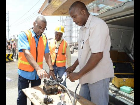 Wayne Marshall (right), engineer at FLOW, repairs cables damaged along Hagley Park Road during expansion work under the MIDP in this 2018 Gleaner photograph. Looking on are Walter Brown (left), vice-president of technology operations at FLOW, and Maurice S