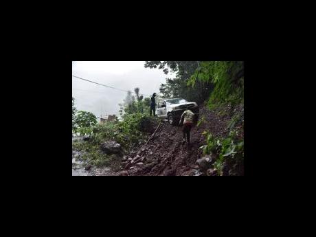 Coffee delivery workers attempting to create a path over a mound of earth to continue on their journey after a landslide along the Mavis Bank main road in St Andrew on Friday.
