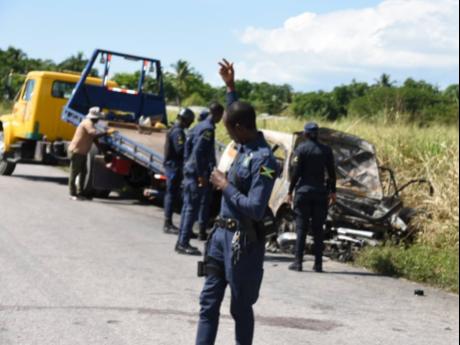 A police officer directs traffic as a wrecker crew prepares to remove the charred car involved in the crash away from the scene on Tuesday morning.
