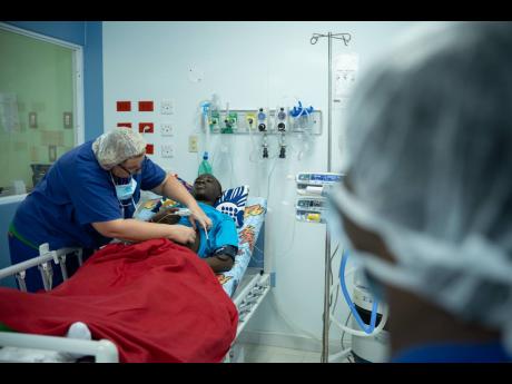 A member of the Chain of Hope UK team examines 14-year-old Nigel Gayle (centre), who received much-needed cardiac surgery, at the Bustamante Hospital for Children in St Andrew yesterday. 