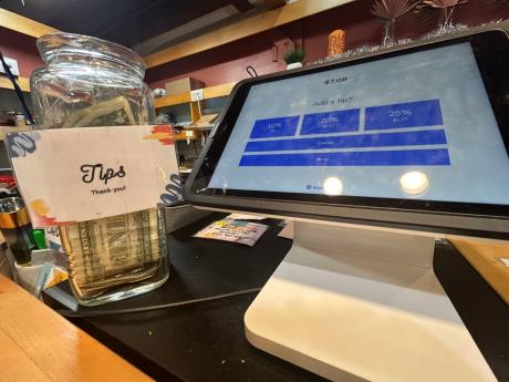 A glass tip jar, left, appears next to a point-of-sale payment system screen displaying tip options at a coffee shop in Waitsfield, Vt, on Wednesday, November 29.
