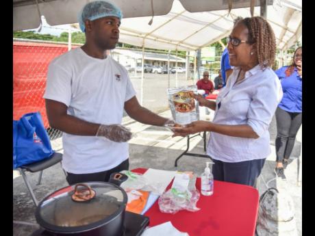 Prep2Pot representative Gavin Dixon (left) hands Faith Webster a pre-prep jerk chicken sample, along with a package of the product, at the SRC Exhibition on Thursday.