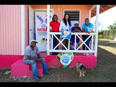 Seventy-six-year-old Enid Walters-Johnson, the first home recipient gifted by the National Baking Company Foundation and Food For The Poor Jamaica for this Christmas season, shares a moment on the verandah of her new home with (from left) neighbour Aston B