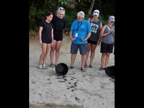 Melvyn ‘Turtleman’ Tennant (centre) from the Oracabessa Bay sea turtle project explains to tourist staying how baby turtles find their way to the sea after birth at the Gibraltar beach in Oracabessa, St Mary, during a turtle release on Thursday.