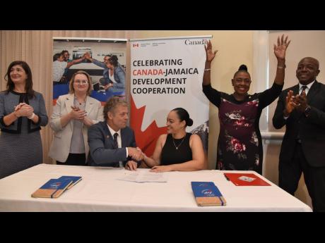 Christian DaSilva (third left), counsellor and head of cooperation for Jamaica at the Canadian Embassy, and Kimberley Sherlock Marriott-Blake (third right), executive director, Jamaica Association for the Deaf, shake hands after the signing of a grant agre