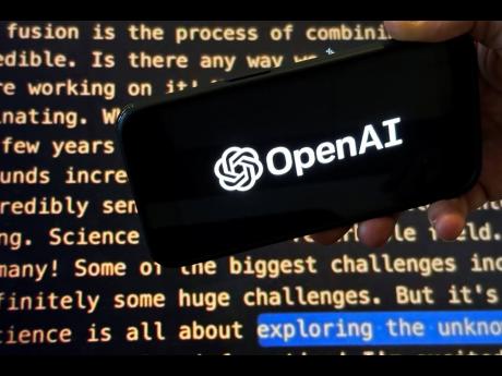 The OpenAI logo appears on a mobile phone in front of a screen showing part of the company website.