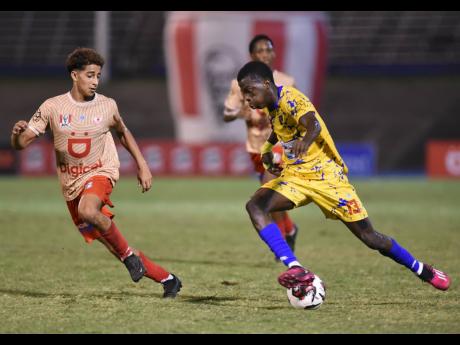 Clarendon College’s Kaheim Dixon (right) tries to dribble by the attentions of Mona High School’s Alex Suazo during their Olivier Shield clash inside the National Stadium last Wednesday. 