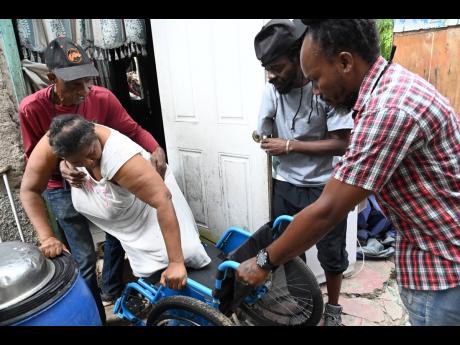 Michael Tulloch (left), director of Greater GIVE Foundation; volunteer Kenroy Graham (second left); and Enroy Thomas, director of Greater GIVE Foundation, assist Vevine Street into her new wheelchair, which they donated, along with Christmas care packages,