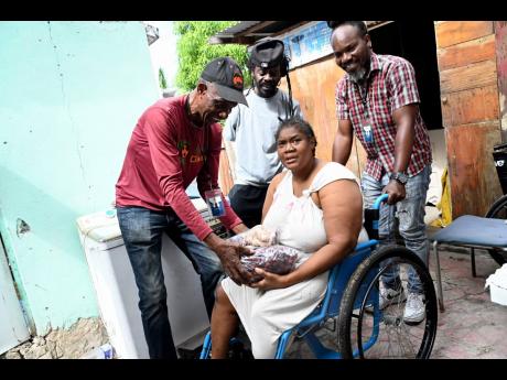 Michael Tulloch (left), director of Greater GIVE Foundation, hands Vevine Street two bags of sorrel and a bag of ginger to brighten her Christmas season as volunteer Kenroy Graham (second left) and Director Enroy Thomas look on.