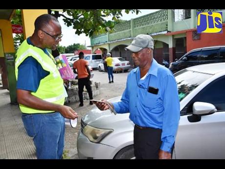 Health promotion and education officer, Westmoreland Health Department, Gerald Miller (left), provides resident of the parish, Errol Spence, with information on dengue fever precautions, during a public education initiative in Savanna-la-Mar on December 15