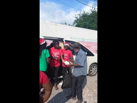 Fifteen-year-old Immaculate Conception High School student Sherinae Brown (second left) getting assistance from Ackeef Nugent (third left) as they present food to needy individuals during her annual Christmas charity Nourishing Neighbours with Helping Hand