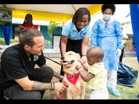 Little Leo Irving, who is a patient at the Bustamante Hospital for Children, pets therapy dog Dr. Teddy Barks, while Curator for the Hope Zoo, Joey Brown (left) and Ear, Nose and Throat (ENT) Consultant and Programme Coordinator for the Animal Assisted Rec