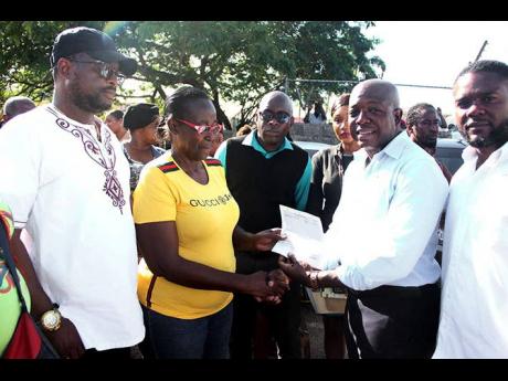 Pearnel Charles Jr (second right), minister of labour and social security, presents Salome Drummond, an Old Shoes Market vendor, with a cheque valued at $60,000 towards her recovery from a fire that destroyed her shop and goods at the facility last October