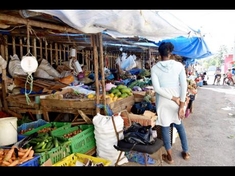 A fruit and vegetable vendor looks at the offerings on the street in Savanna-la-Mar, outside the municipal market, on Thursday.