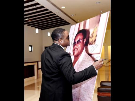Robert Hendricks Jr, son of the late tourism mogul Robert Hendricks, looks deeply at a picture of his father during the funeral for the senior Hendricks at the Montego Bay Convention Centre on Sunday, January 28.