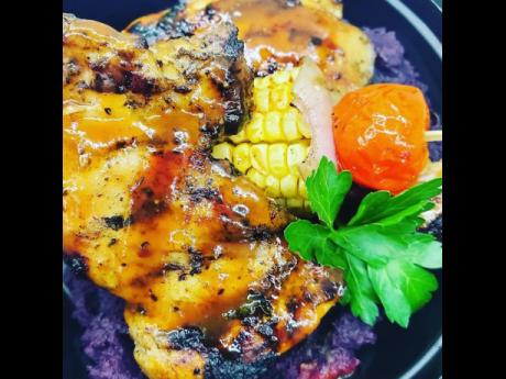 Presented on a bed of purple sweet potatoes and accompanied by corn on the cob and assorted vegetables. This flavourful jerk chicken is a delicious treat.
