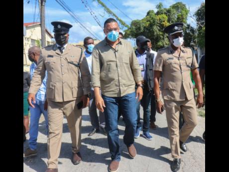 Prime Minister Andrew Holness walks with (left) Deputy Superintendent Adrian Hamilton and Assistant Commissioner Clifford Chambers on the Ricketts and Dexter streets in Savanna-La-Mar, Westmoreland. This is due to the parish being the epicenter of crime.