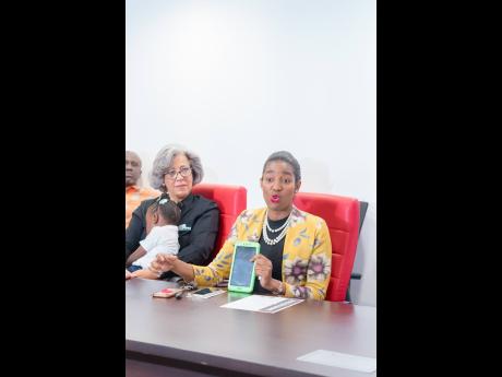  Gracie Moss-Solomon (right), principal, Union Gardens Infant School, addresses the gathering as Kim Mair, chief executive officer, JMMB Joan Duncan Foundation, holds a sleeping Adrianna McKnight during yesterday’s launch of the One Tab In Schools Initia