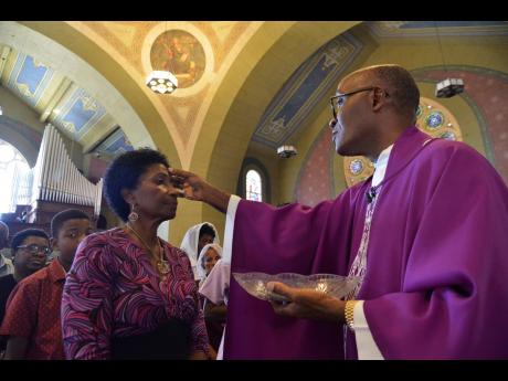 In this 2019 photo, Rev Kingsley Asphall from The Holy Trinity Cathedral, North Street in Kingston, makes ash cross sign on Sharon Asphall on Ash Wednesday.