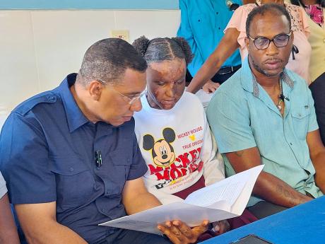 Prime Minister Andrew Holness (left) examines the terms of the government’s new social housing programme contract with Adrianna Laing and her father Adrian Laing in Slope, St Elizabeth yesterday.