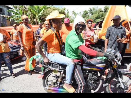 A JLP supporter gives a ride to a PNP supporter on his bike in Kellits, Clarendon Northern, on nomination day.
