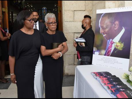 Gisele Gibson (left) and her mother Janet Morrison, wife of the late Justice C. Dennis Morrison, exit The University Chapel with the urn bearing his remains after a funeral on Thursday.