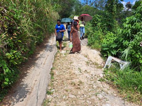 Residents of Freeman’s Hall, Trelawny, walking along a section of the community’s main road, which they say has not been adequately addressed for 50 years.