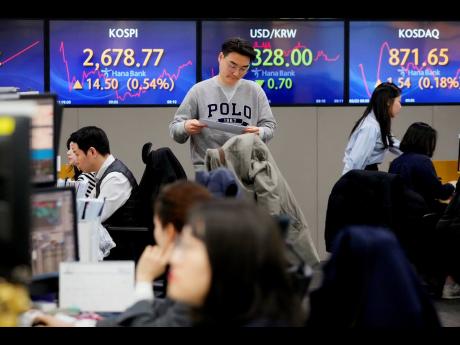 A currency trader passes by the screens showing the Korea Composite Stock Price Index (left) and the foreign exchange rate between the US dollar and South Korean won (centre), at the foreign exchange dealing room of the KEB Hana Bank headquarters in Seoul,