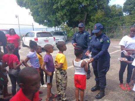 Woman Constable  Chevoy McKoy presents bun and cheese to a student at the Jubilee Primary School,while Sgt Kenneth McTavish and others look on.