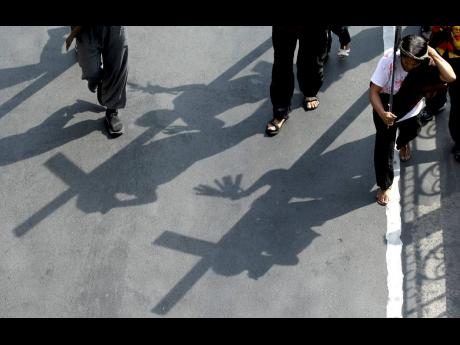 This 2018 photos shows shadows of protesters carrying wooden crosses are reflected on the street as they re-enact the sufferings of Jesus Christ during a rally on holy week in Manila, Philippines.