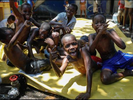 Children react to the camera as they play on a slip-and-slide at a shelter for families displaced by gang violence in Port-au-Prince.